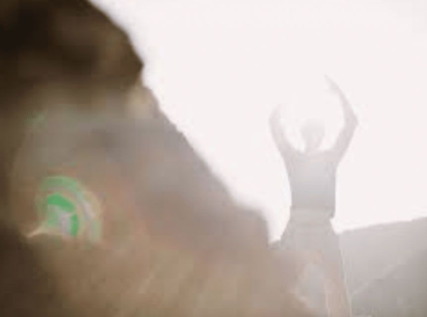 Person with arms raised in bright, hazy outdoor light