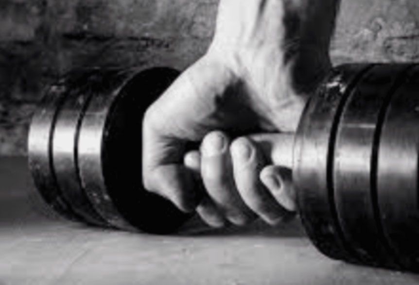 Hand gripping a dumbbell on a gym floor, with another dumbbell beside it