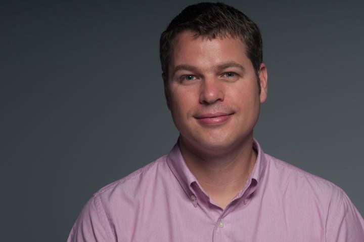 Portrait of a man in a pink shirt against a dark gray background