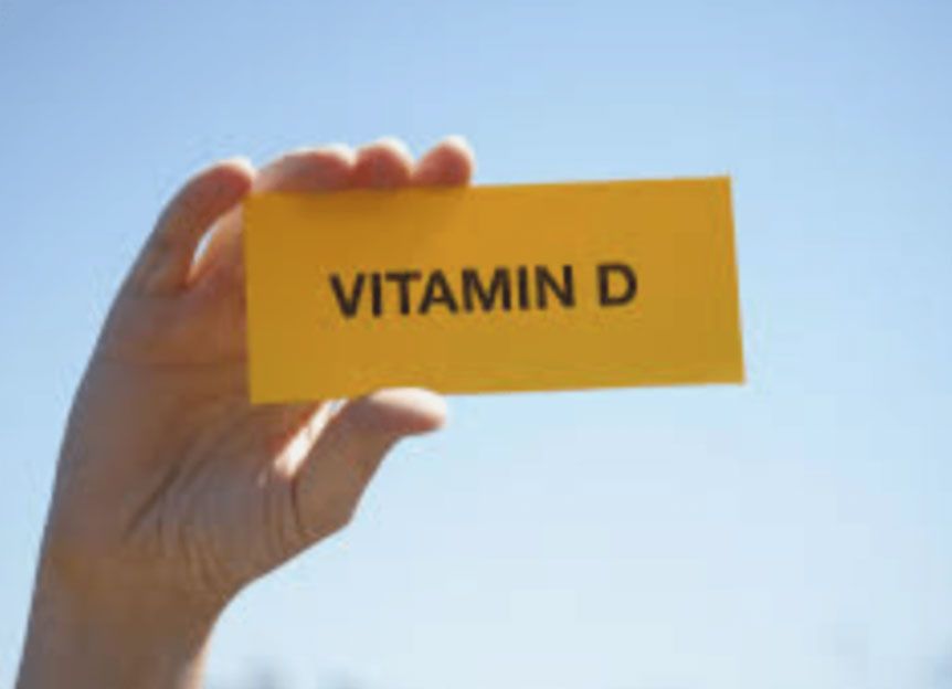 Hand holding a yellow card labeled “VITAMIN D” against a blue sky.