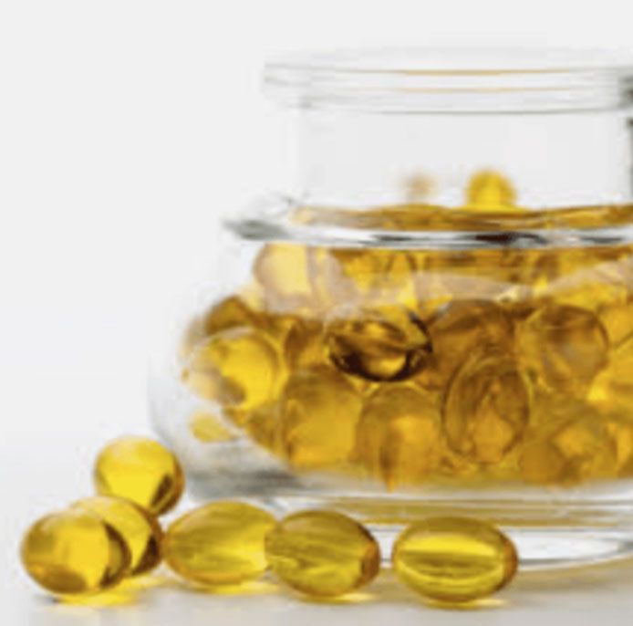 Transparent jar and scattered golden capsules on a white background