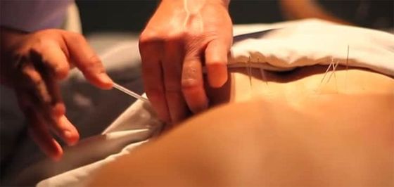 Hands adjusting a white sheet on a person’s back during a massage or therapy session