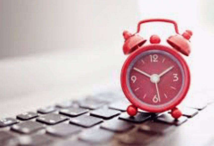 Red alarm clock on a laptop keyboard, symbolizing time pressure or deadlines