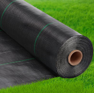 A roll of black weed barrier is sitting on top of a lush green field.