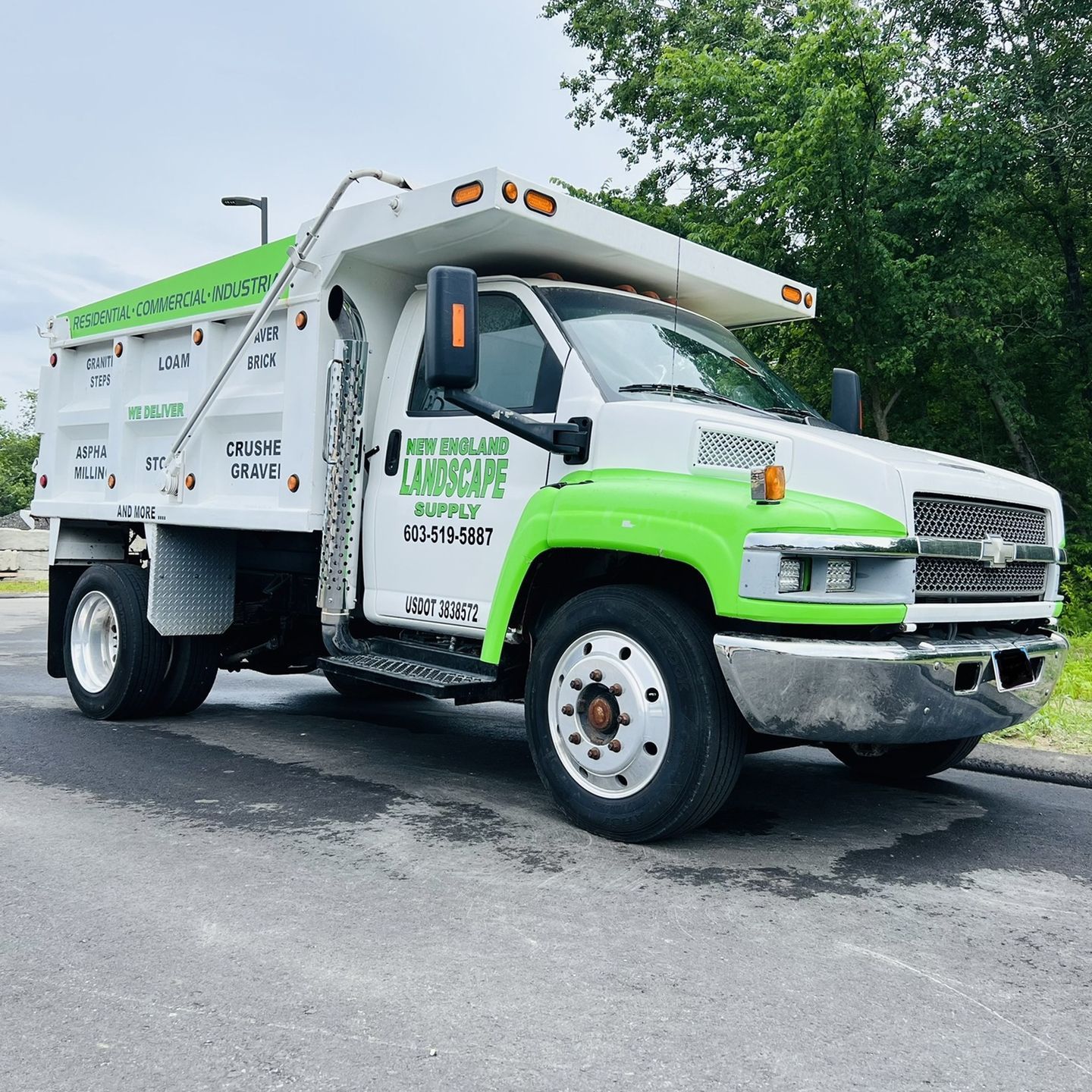 A white and green dump truck is parked on the side of the road.