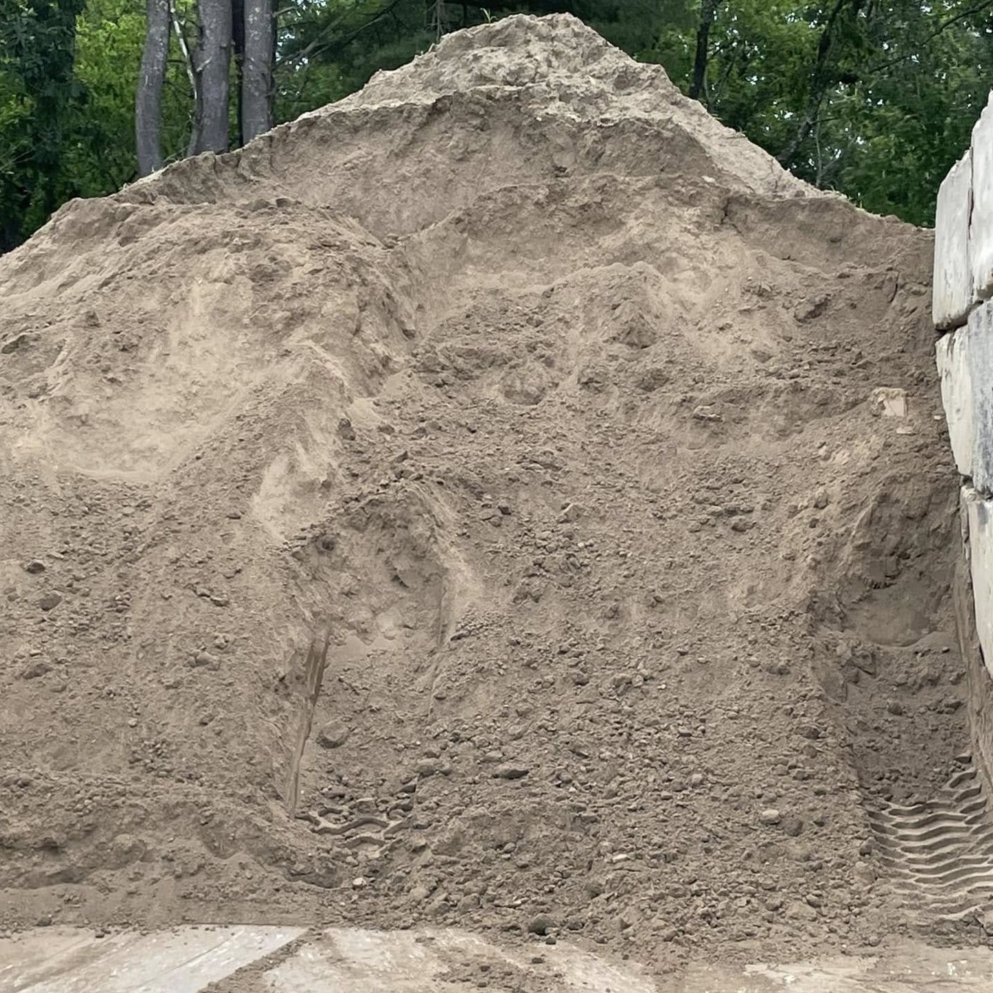 A large pile of dirt is sitting next to a concrete wall.
