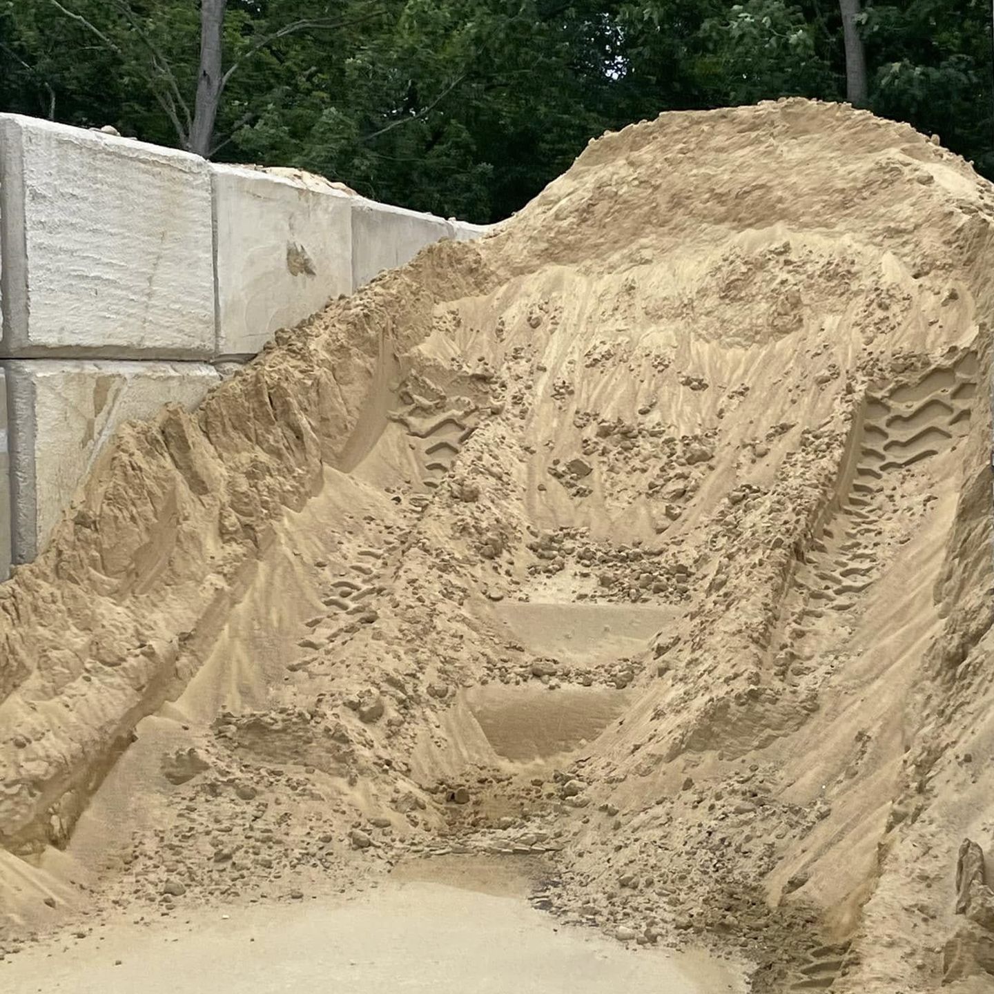 A pile of sand is sitting in front of a concrete wall.