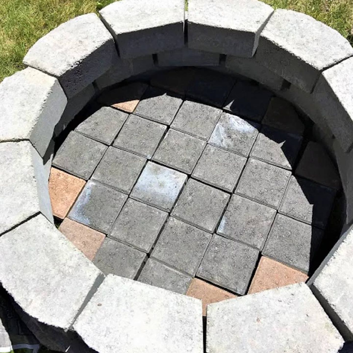A fire pit made of bricks is sitting in the grass.