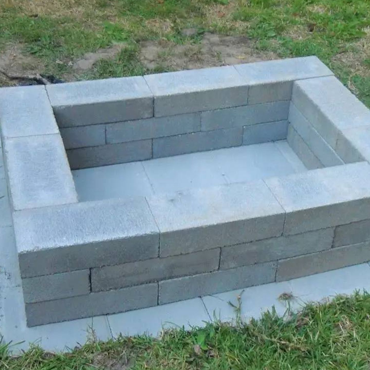 A fire pit made out of concrete blocks is sitting in the grass.