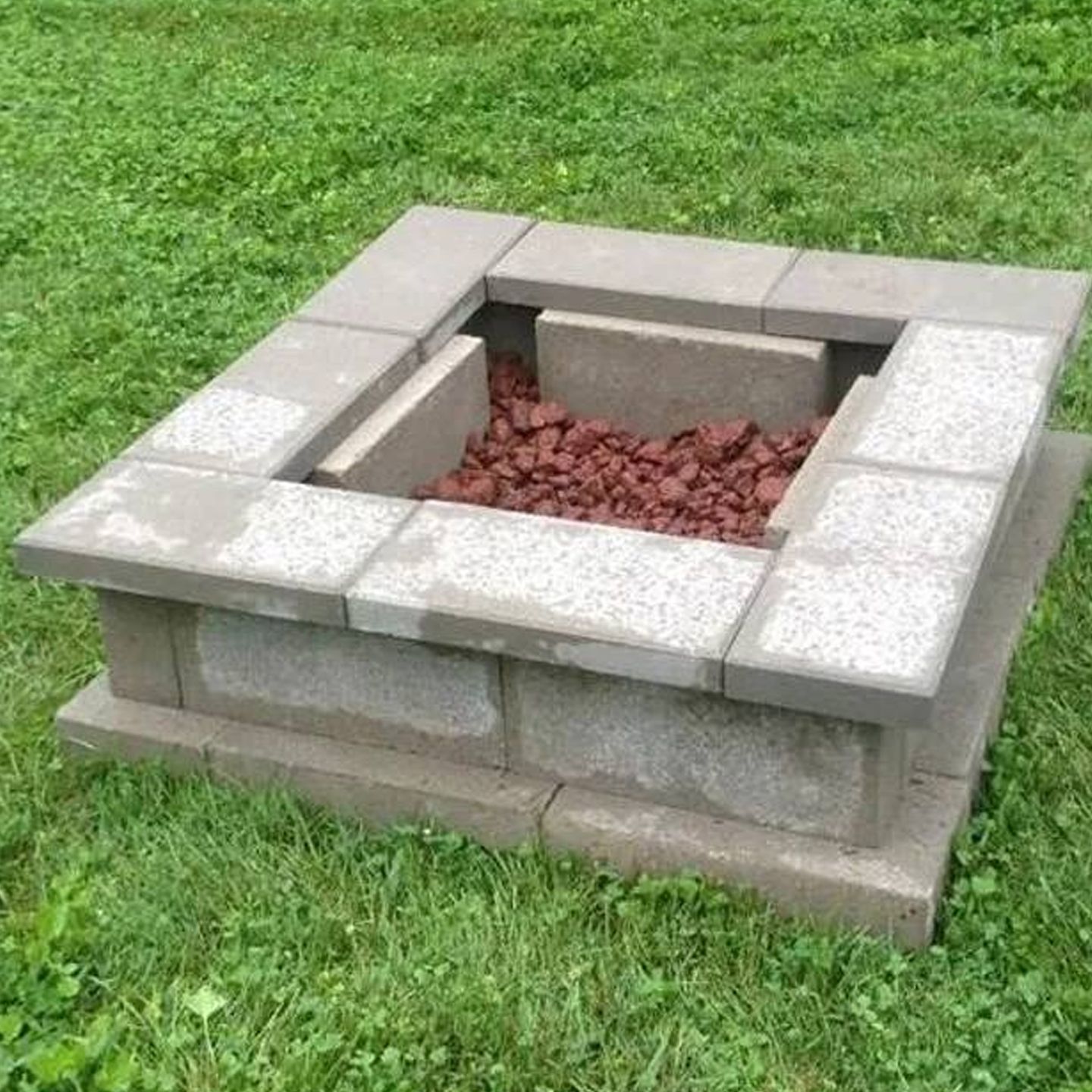 A fire pit is sitting in the middle of a lush green field.