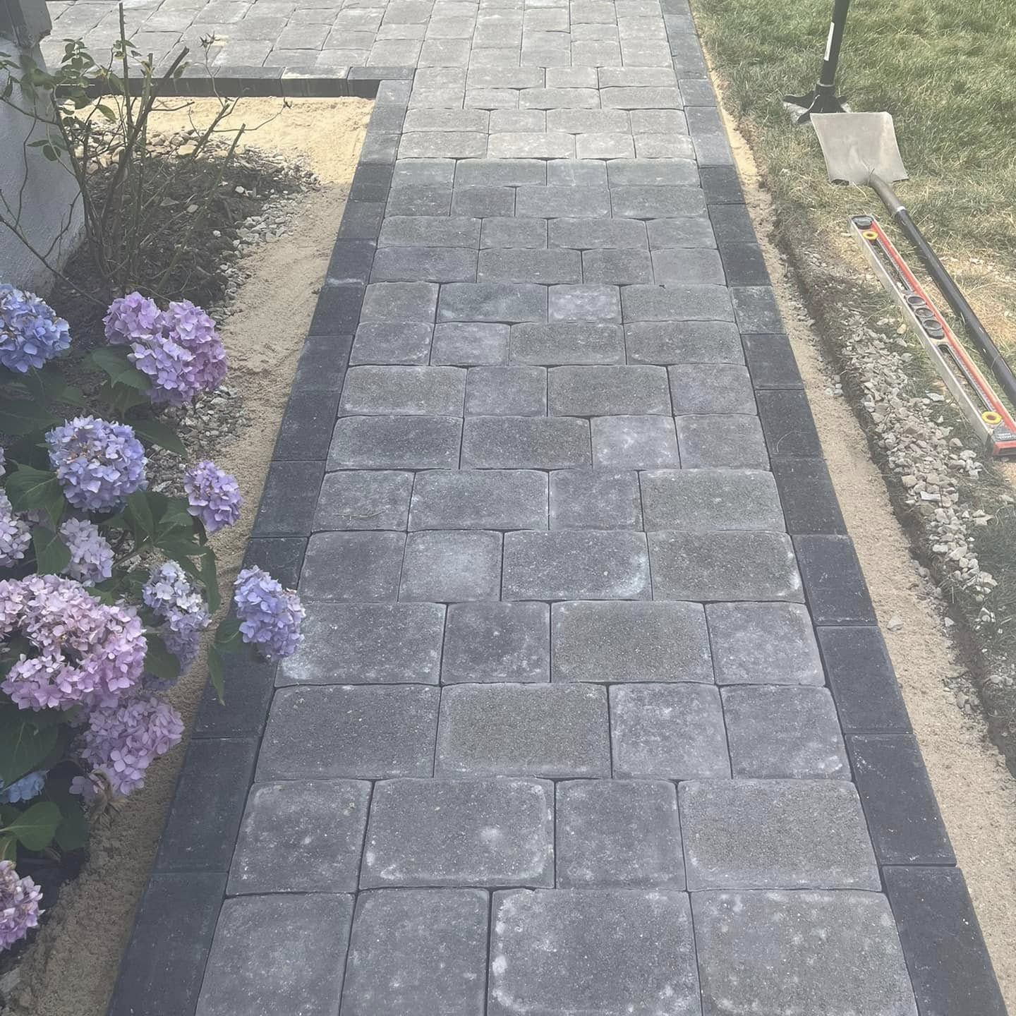A brick walkway with purple flowers on the side