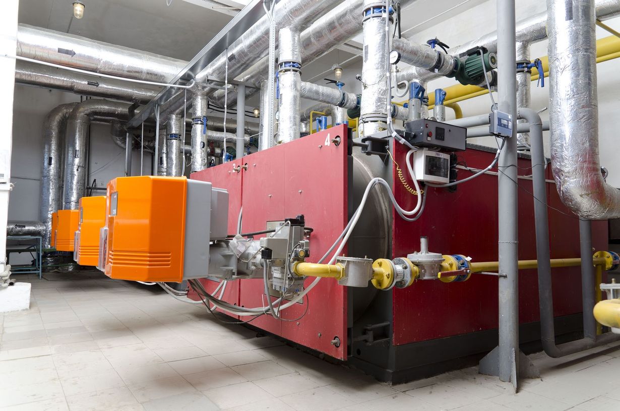 A large red boiler is sitting in a warehouse surrounded by pipes.