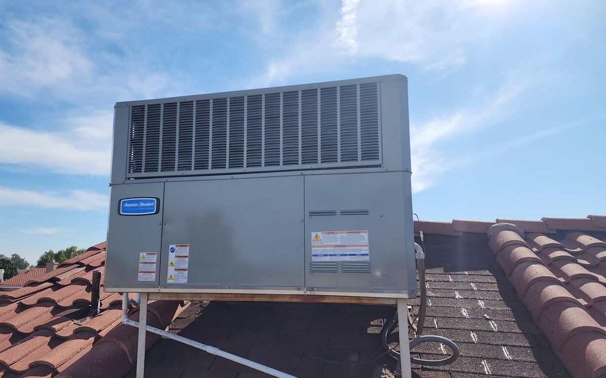 A large air conditioner is sitting on top of a tiled roof.