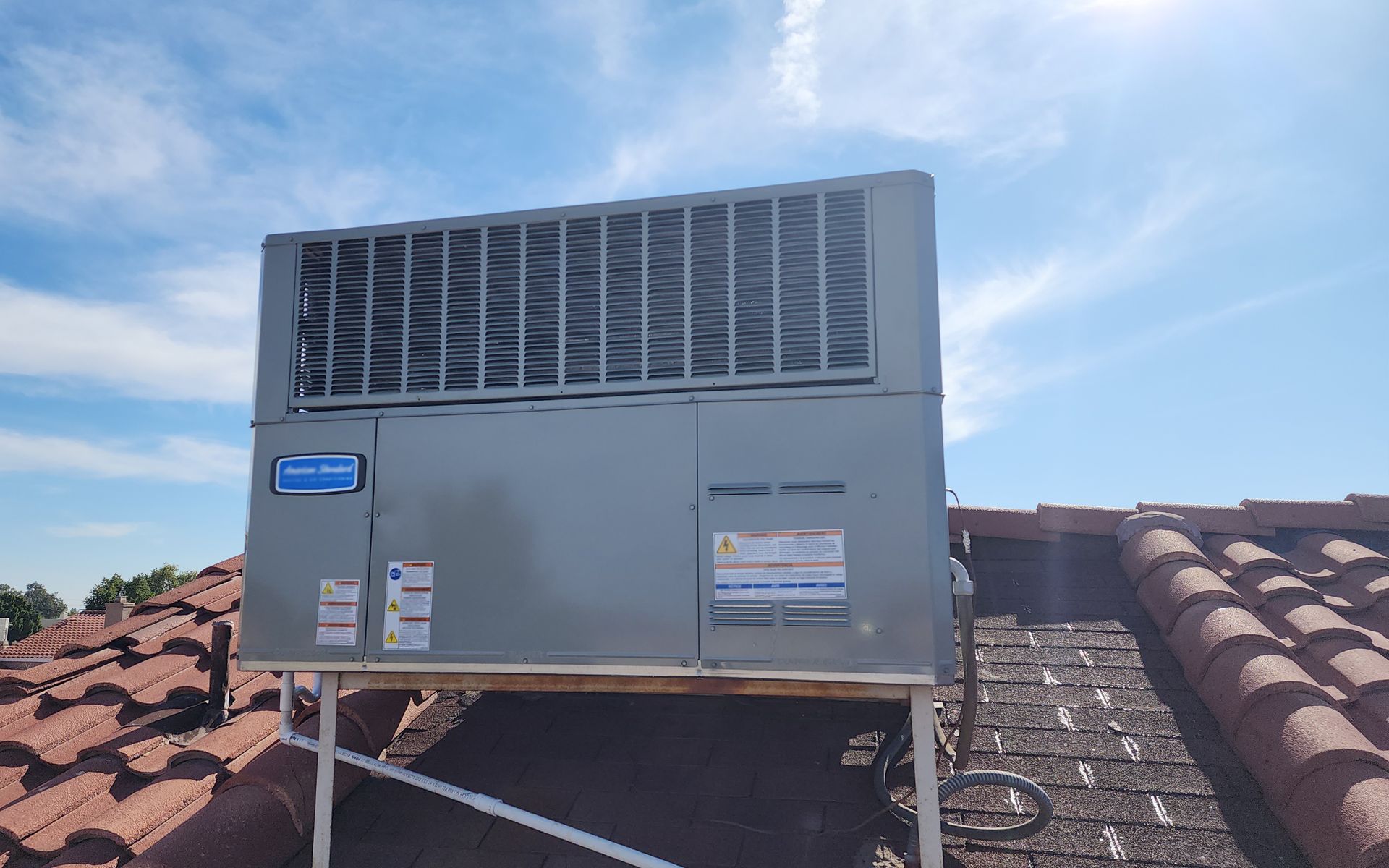 A large air conditioner is sitting on top of a tiled roof.