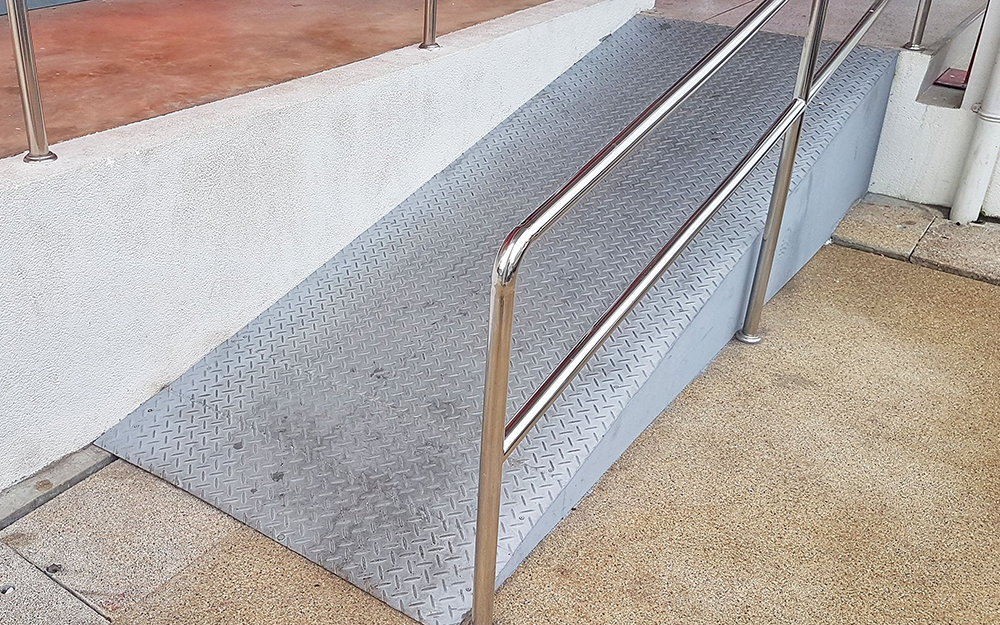 A ramp with a stainless steel railing is next to a set of stairs