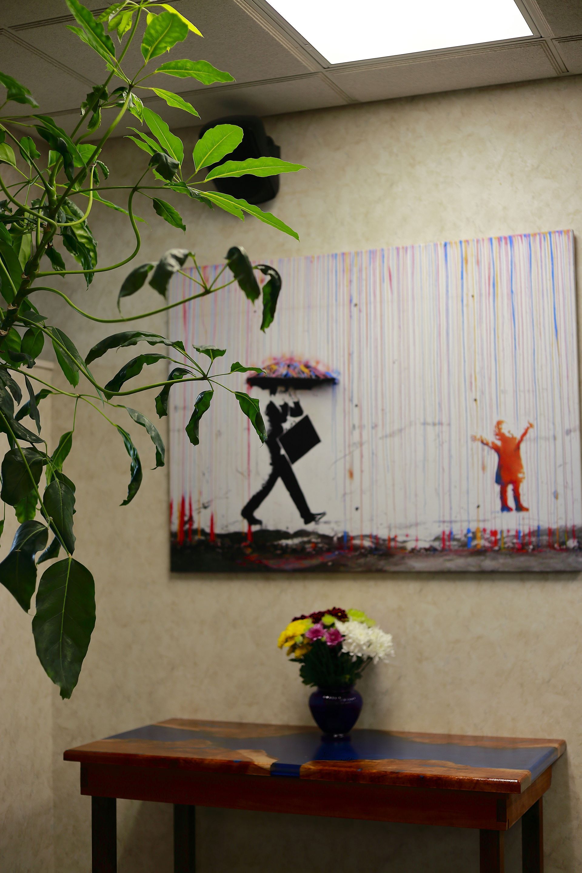A table with a vase of flowers and a painting on the wall above it