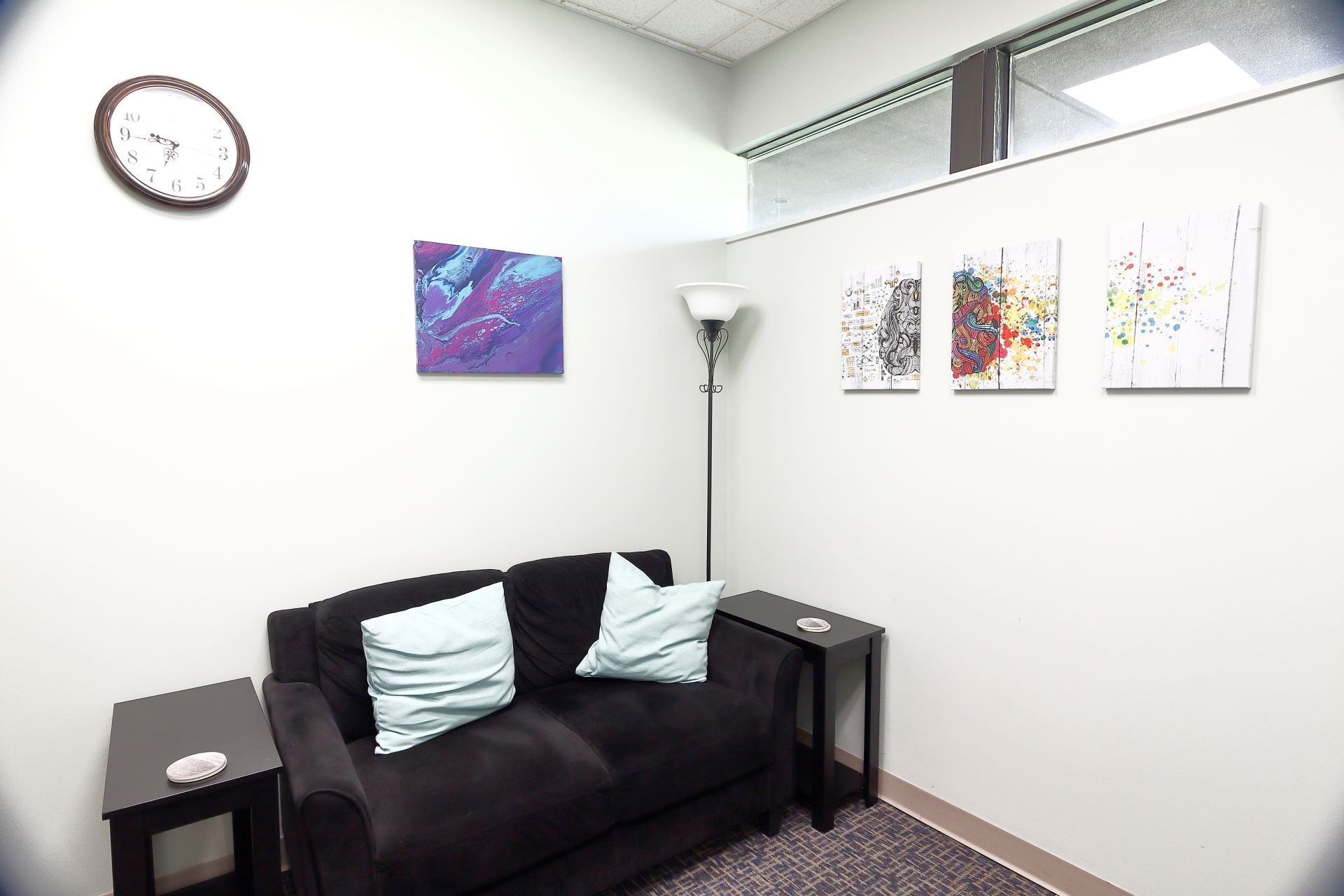 A living room with a black couch and a clock on the wall.