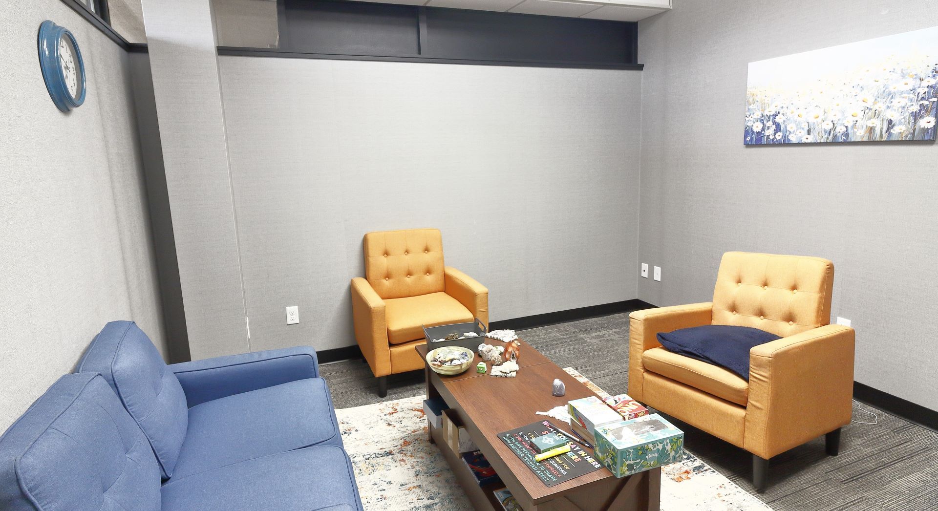 A living room with a blue couch , two chairs , a coffee table and a clock on the wall.