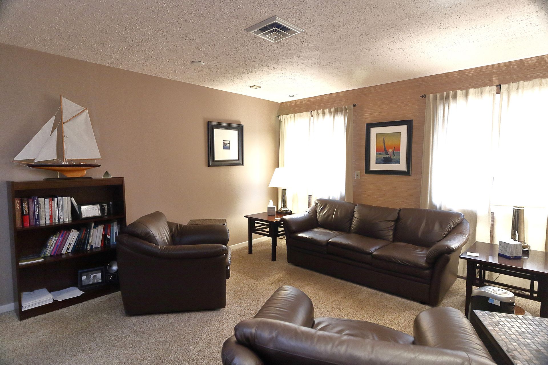 A living room with brown furniture and a sailboat on the wall. - Andy