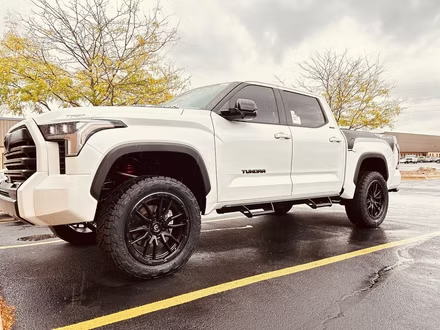 White Toyota Tacoma pickup truck parked on a wet road with autumn trees in the background