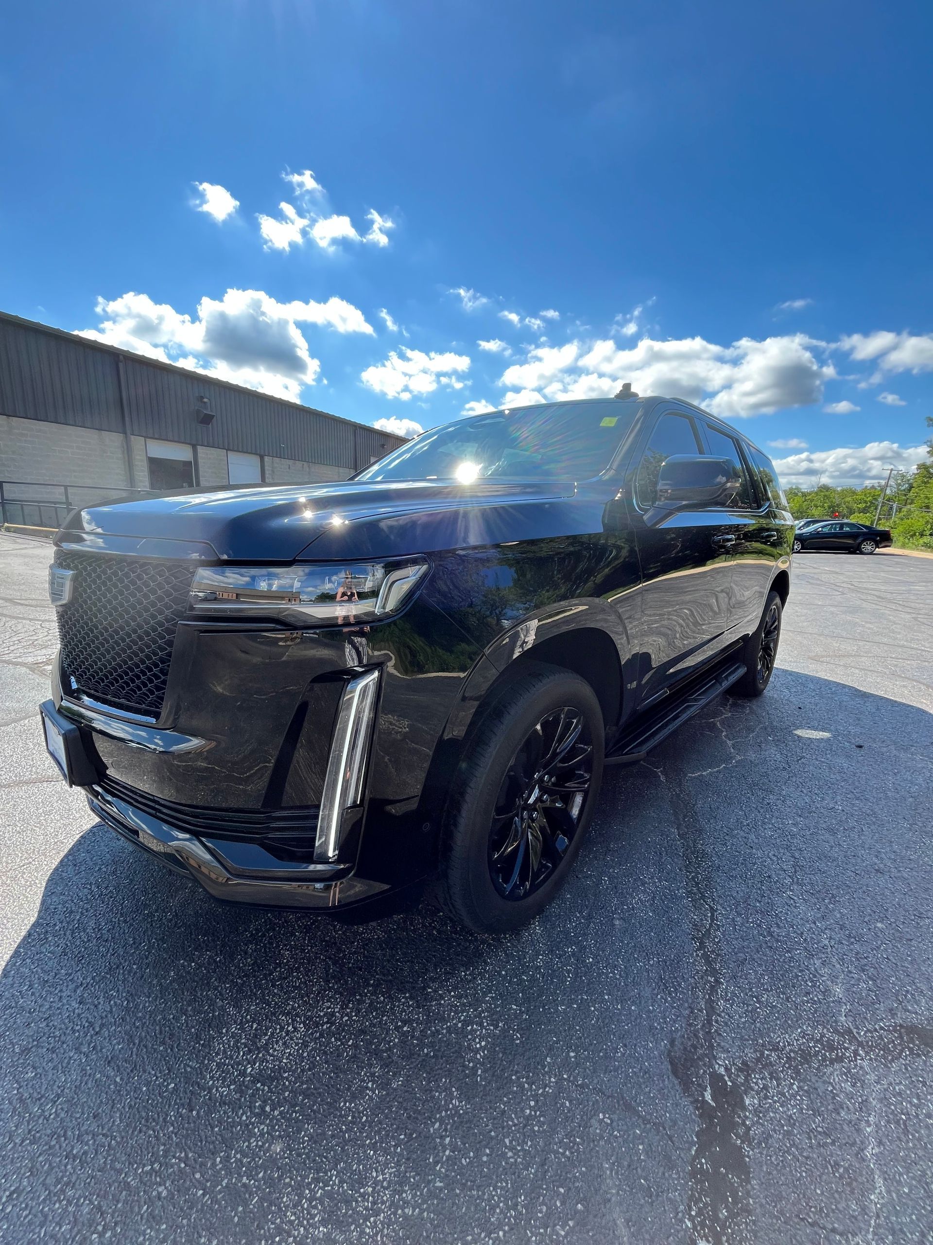 Black SUV parked on a sunny lot under a blue sky with scattered clouds