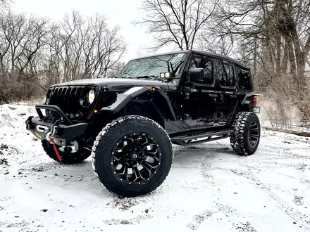 Black off-road Jeep with large tires parked on a snowy trail in a bare winter woods