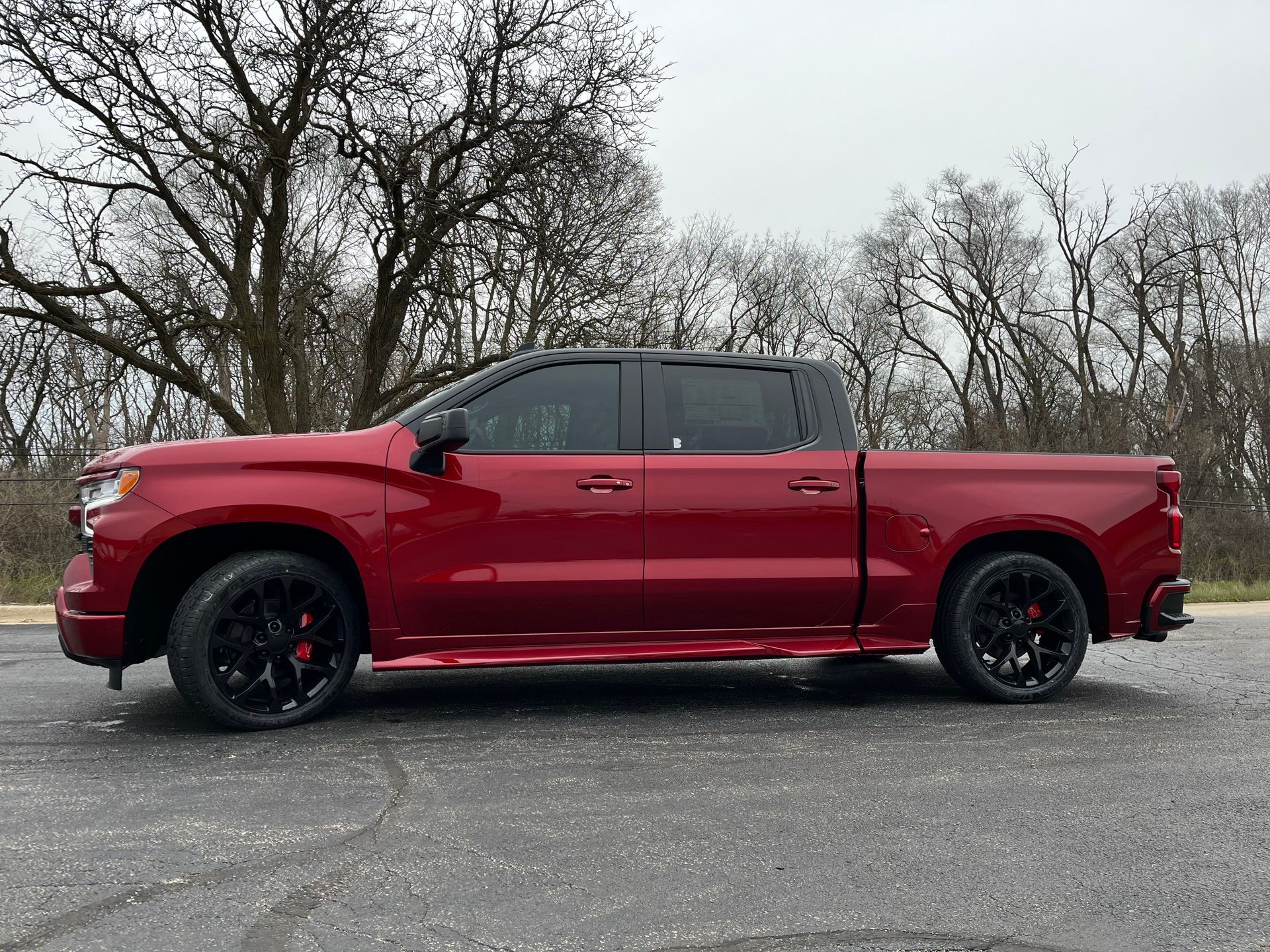 Red lifted pickup truck parked outdoors on pavement, side view with trees in the background