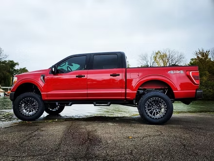Red lifted crew cab pickup truck parked on wet pavement under a cloudy sky