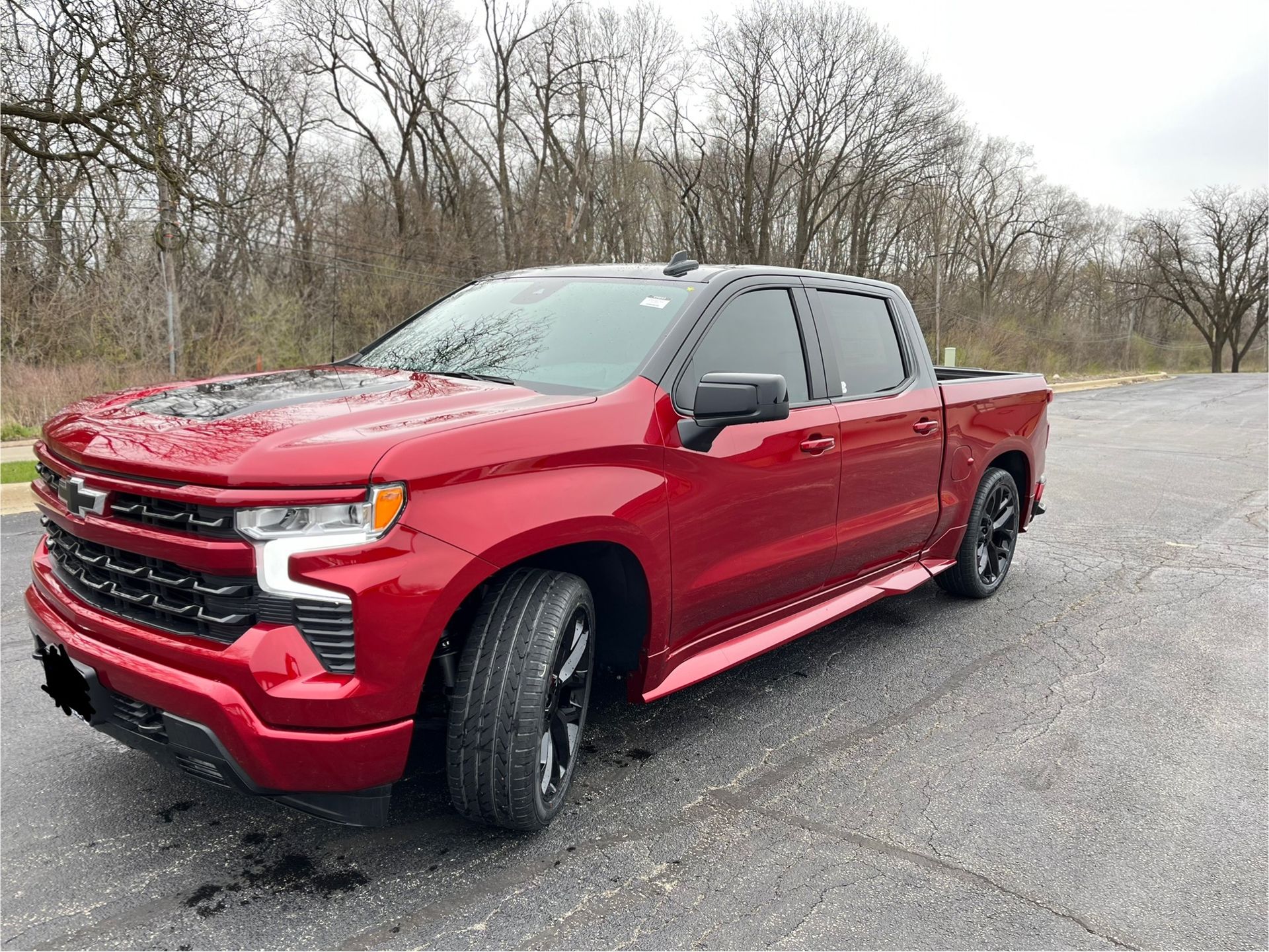 Red pickup truck parked on a wet road beside leafless trees