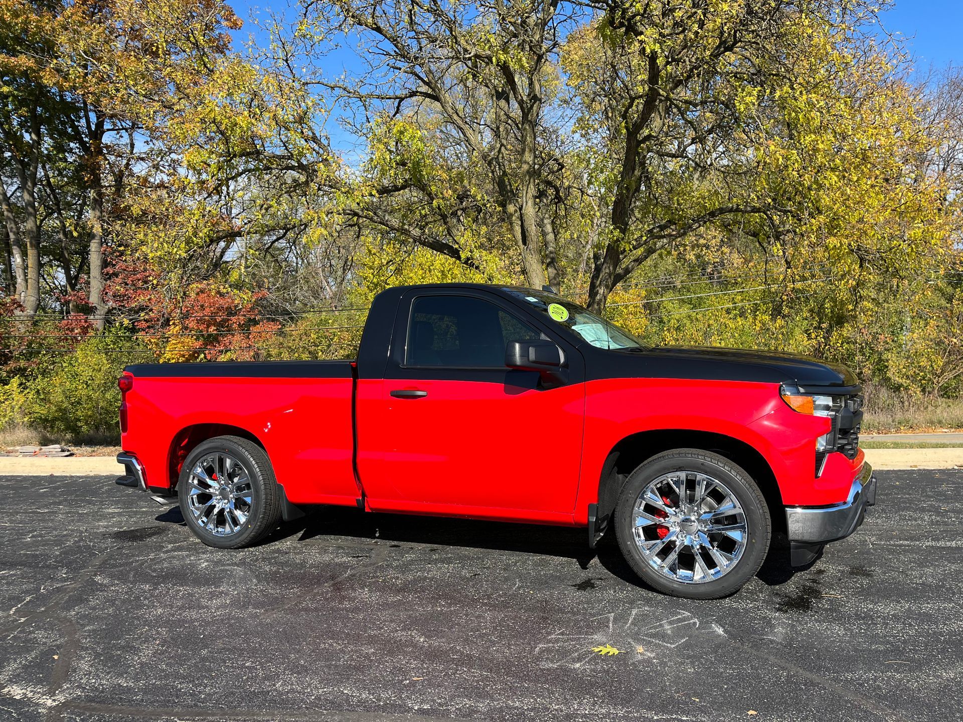 Red pickup truck parked on asphalt in front of trees with fall foliage
