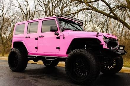 Bright pink lifted Jeep SUV with black wheels parked on a wet road under bare trees.