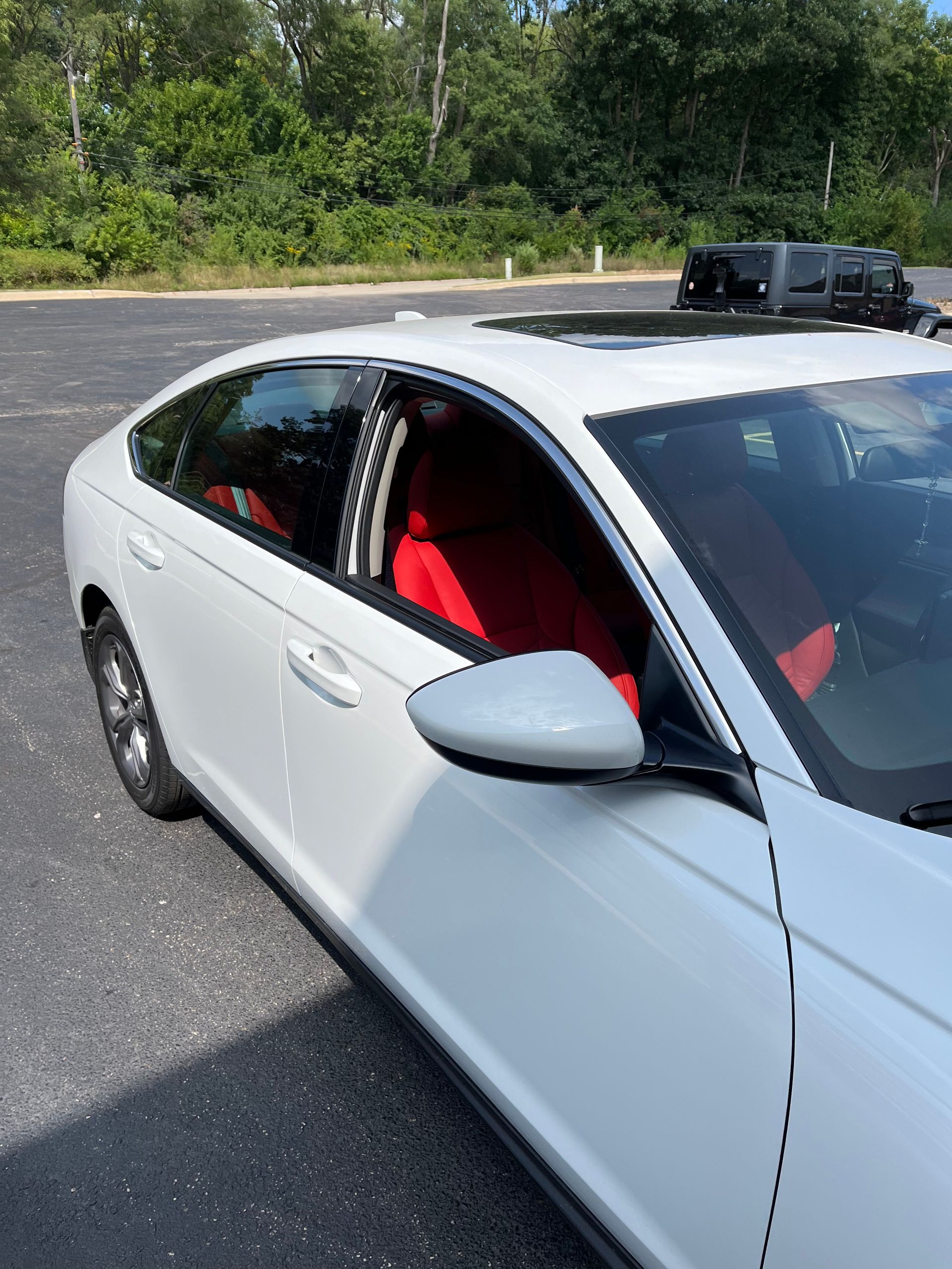White sedan with open window and red seats parked beside a road