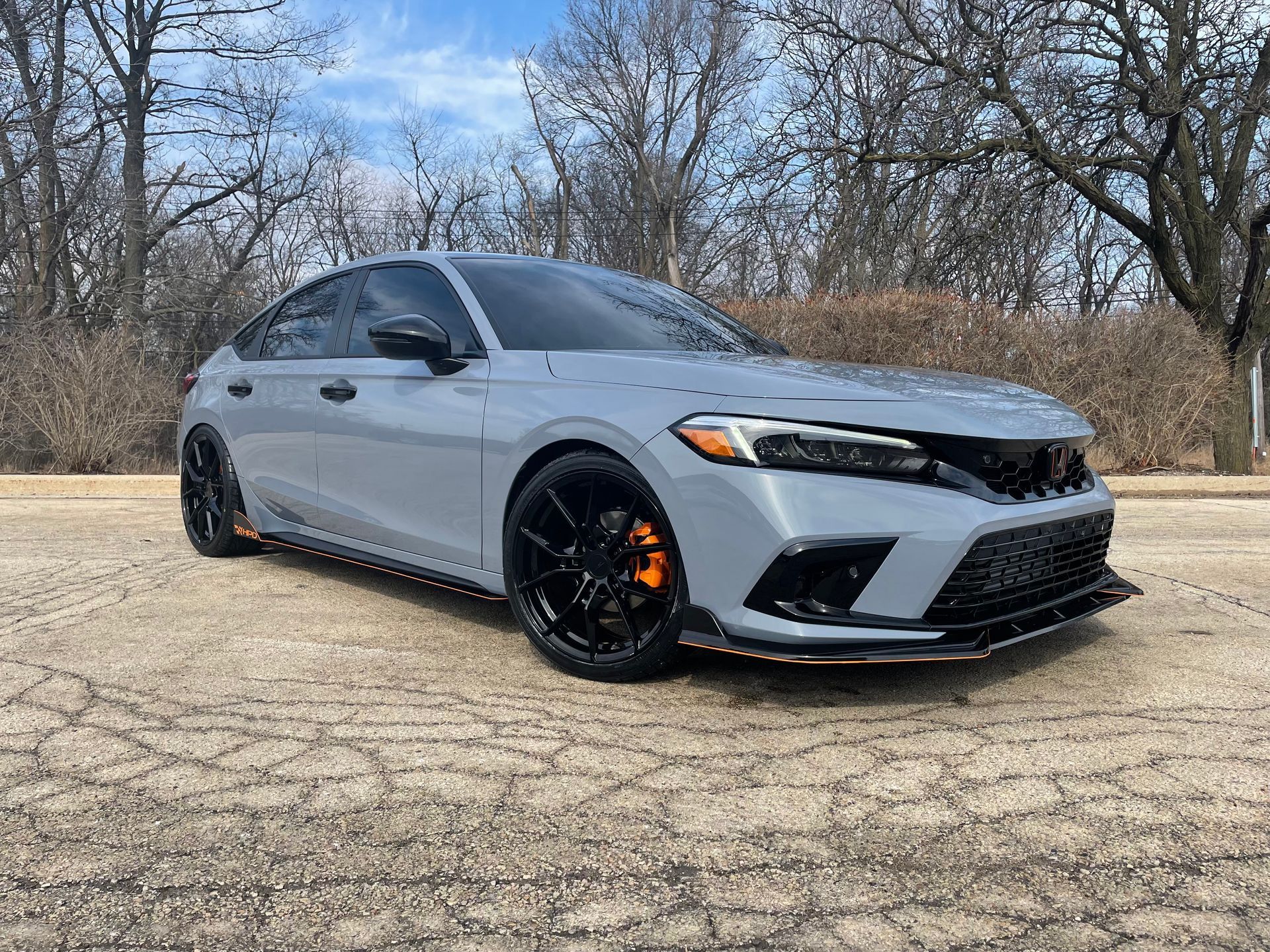Silver sedan with black wheels parked on a road beside leafless trees