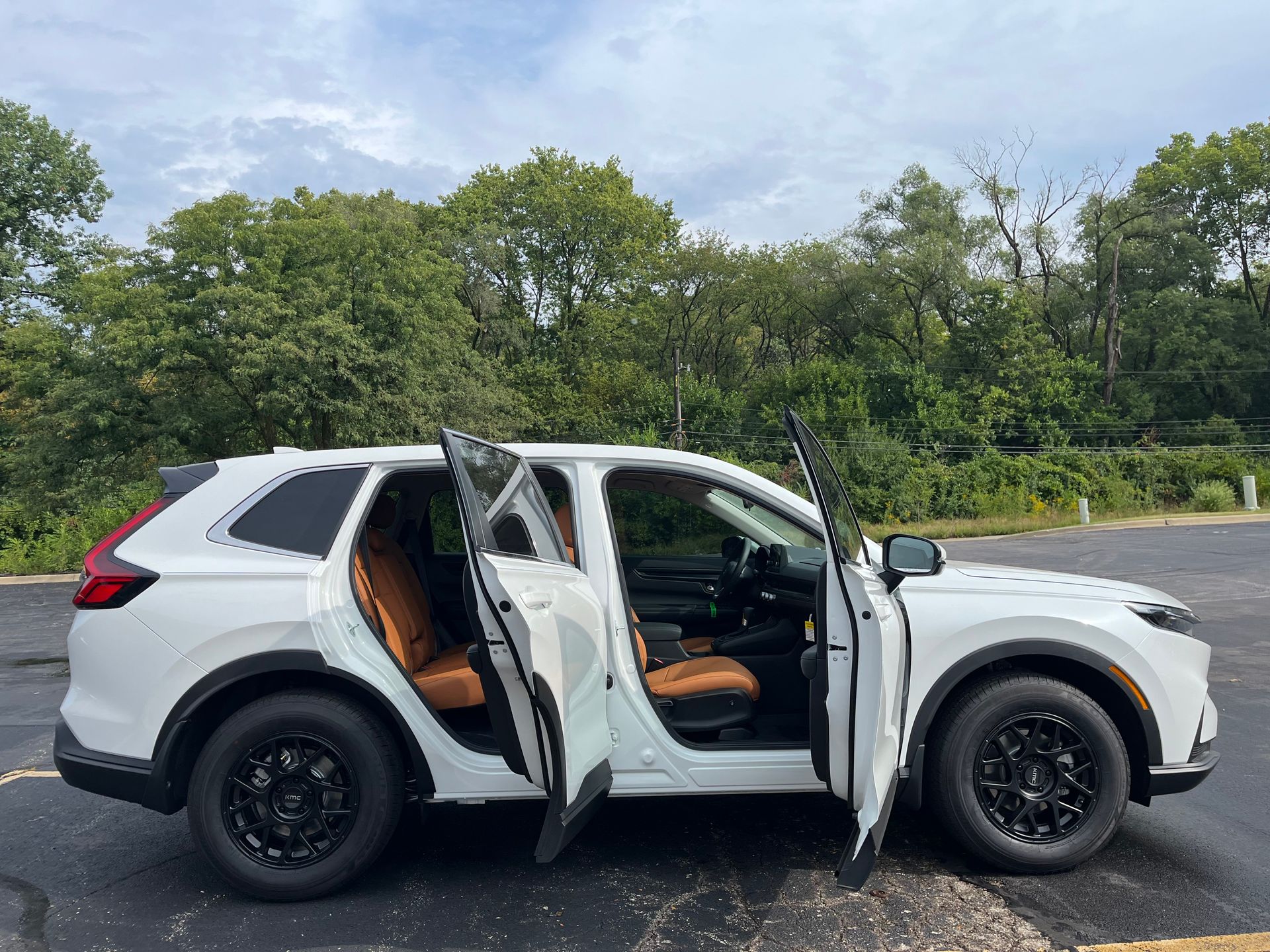 White SUV with both passenger-side doors open on a road beside trees and greenery