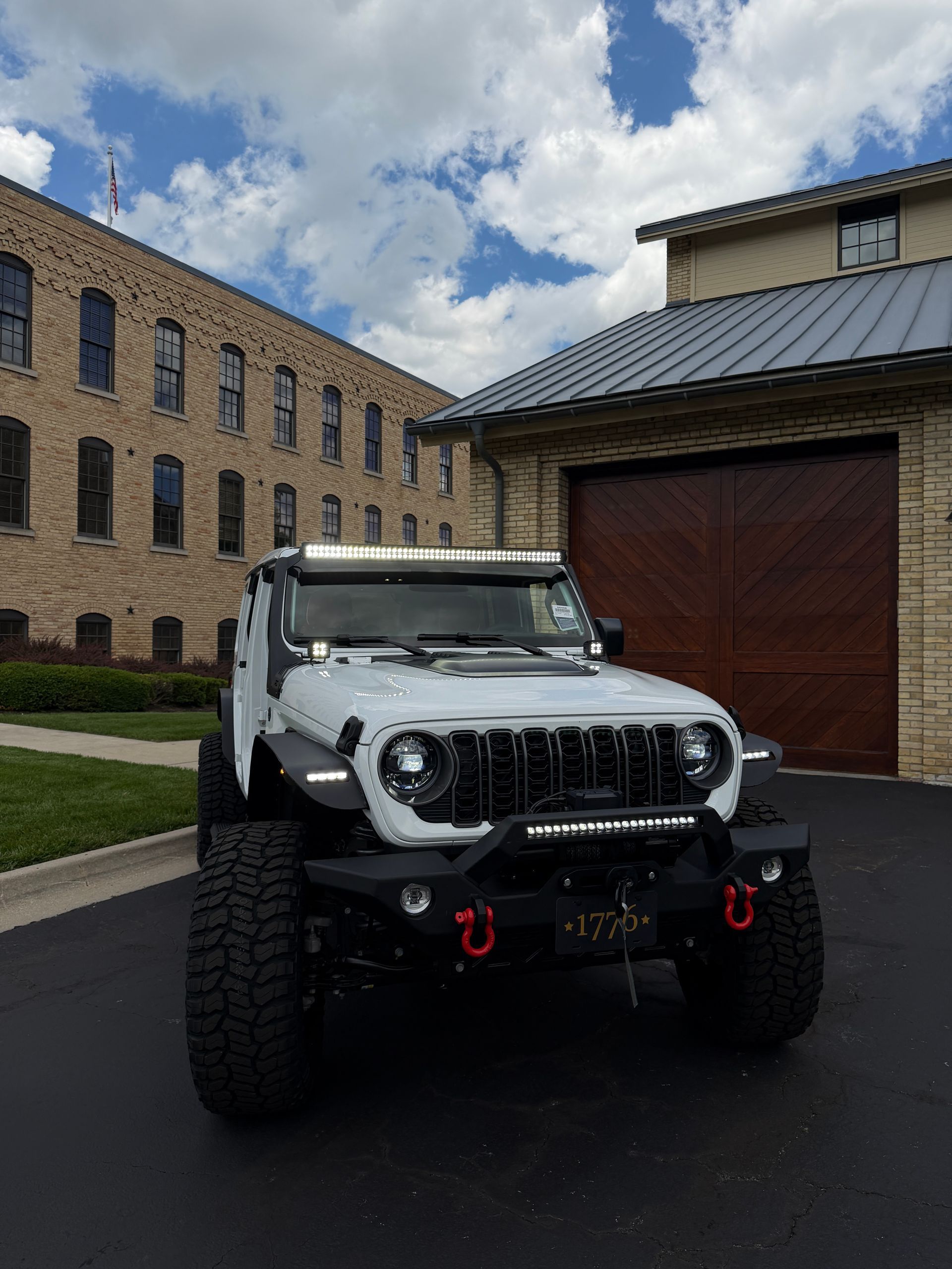 White Jeep Wrangler parked on wet pavement beside brick buildings and a garage door