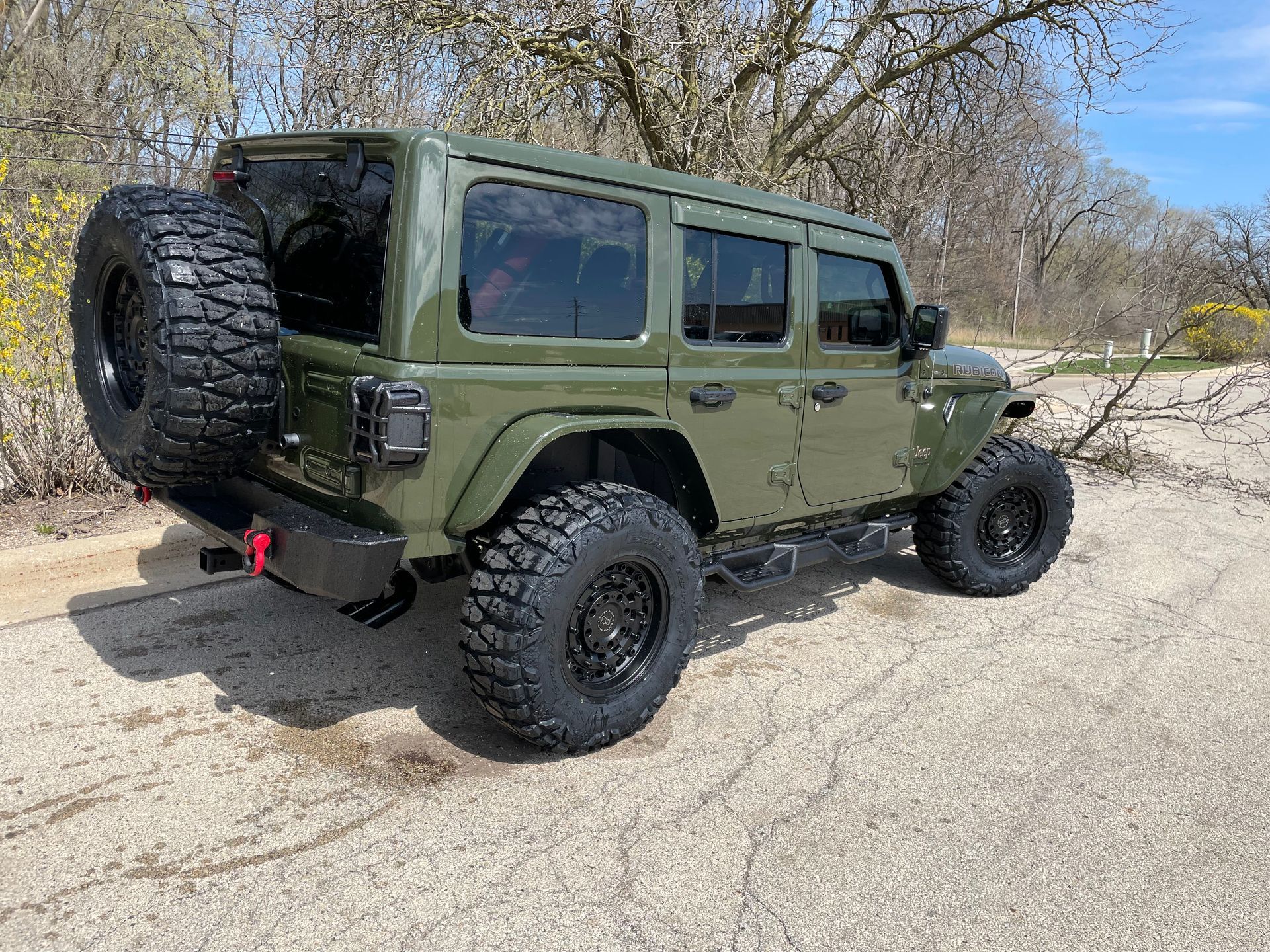Green off-road Jeep with large tires parked on a sandy trail near bare trees