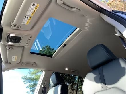 Car interior with sunroof open, showing blue sky and a gray headliner above the front seats.