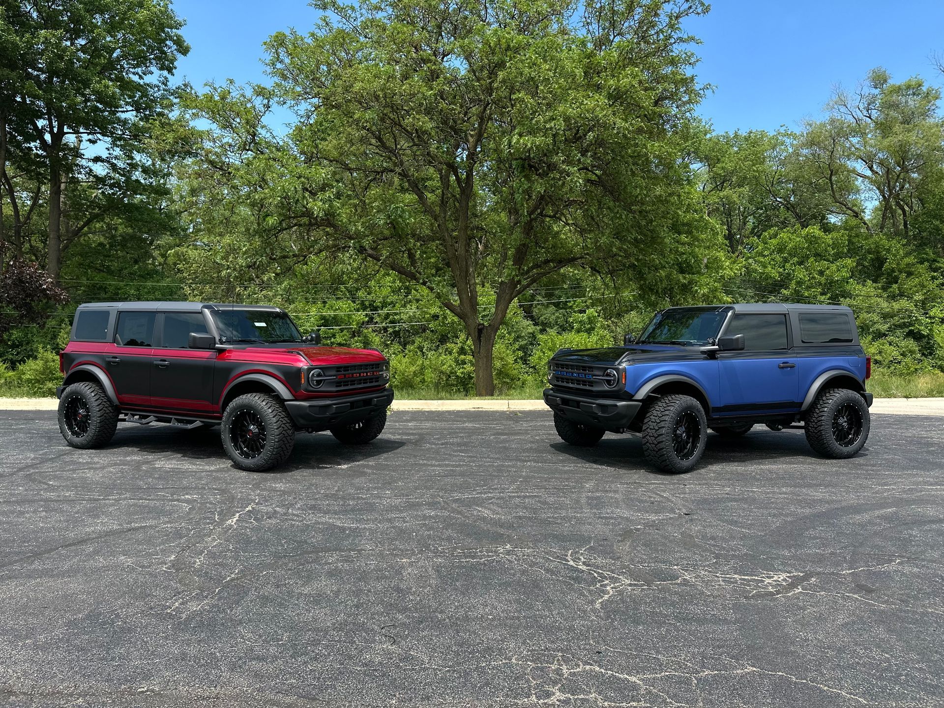 Two rugged SUVs, one red and one blue, parked on a gravel lot with trees in the background