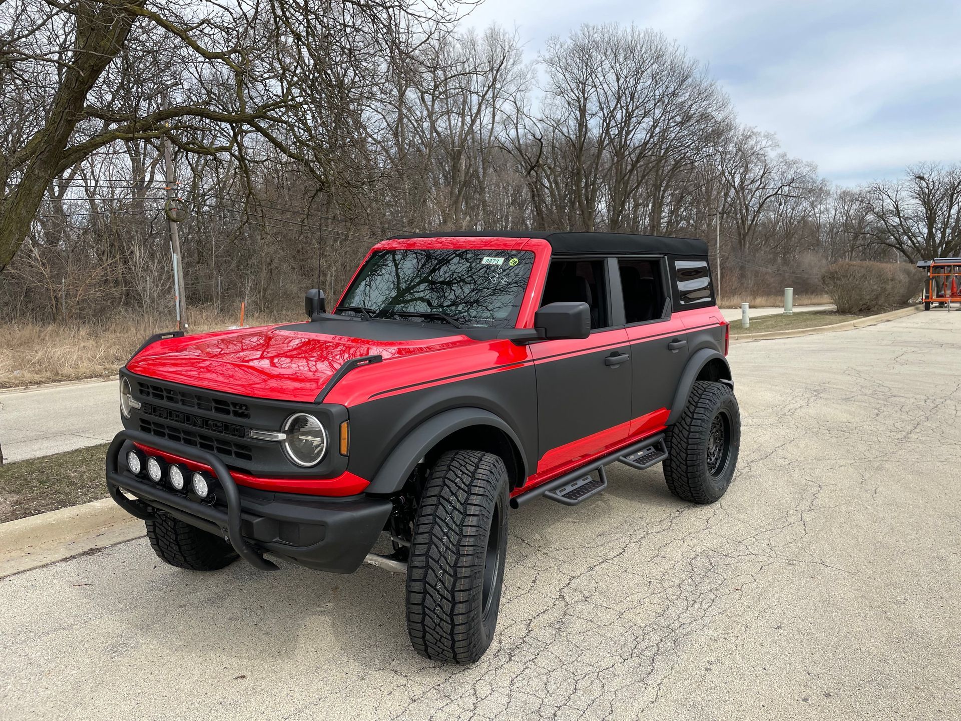 Red off-road SUV with black accents parked on a roadside with bare trees in the background