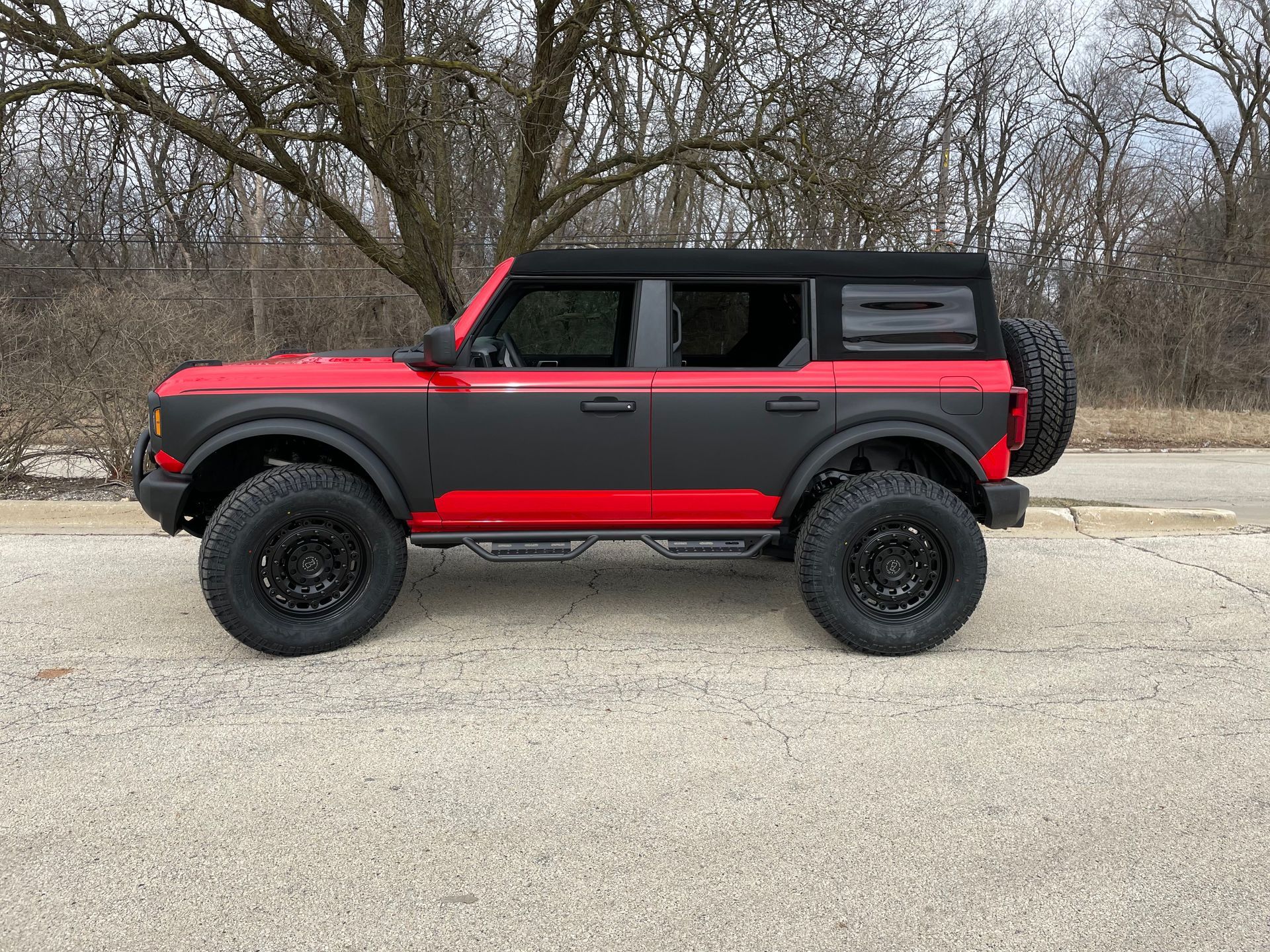 Red and black off-road SUV parked on a gravel road with bare trees in the background
