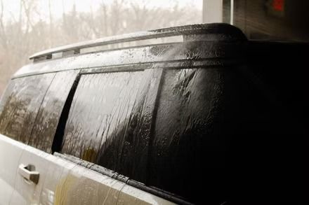 Rain-soaked black SUV window with water streaming down the glass