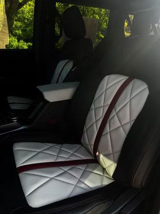 White quilted car seat cover with red trim in a vehicle interior, sunlight streaming through the window