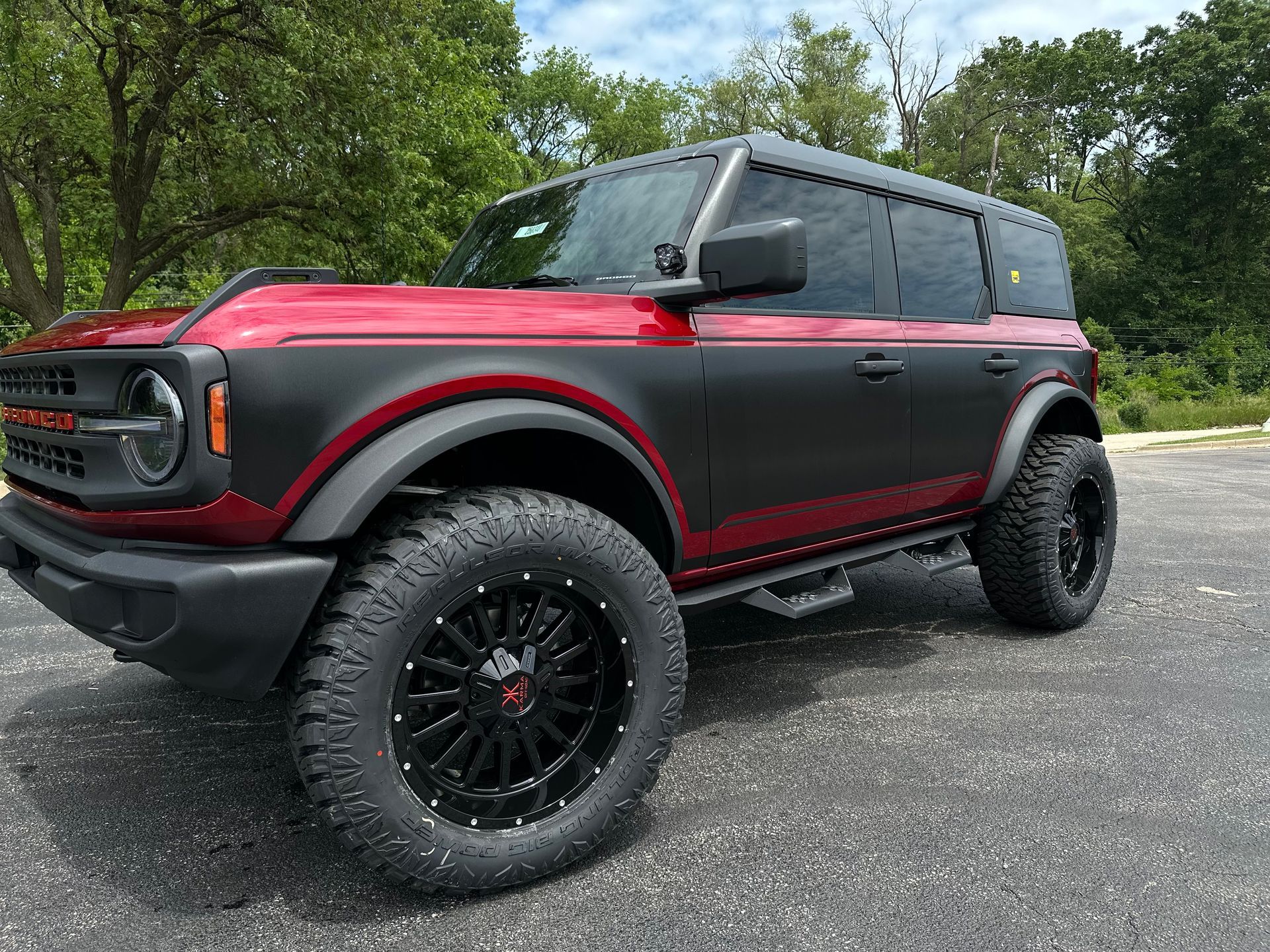 Red off-road SUV with black accents and large tires parked on a gravel road beside trees.