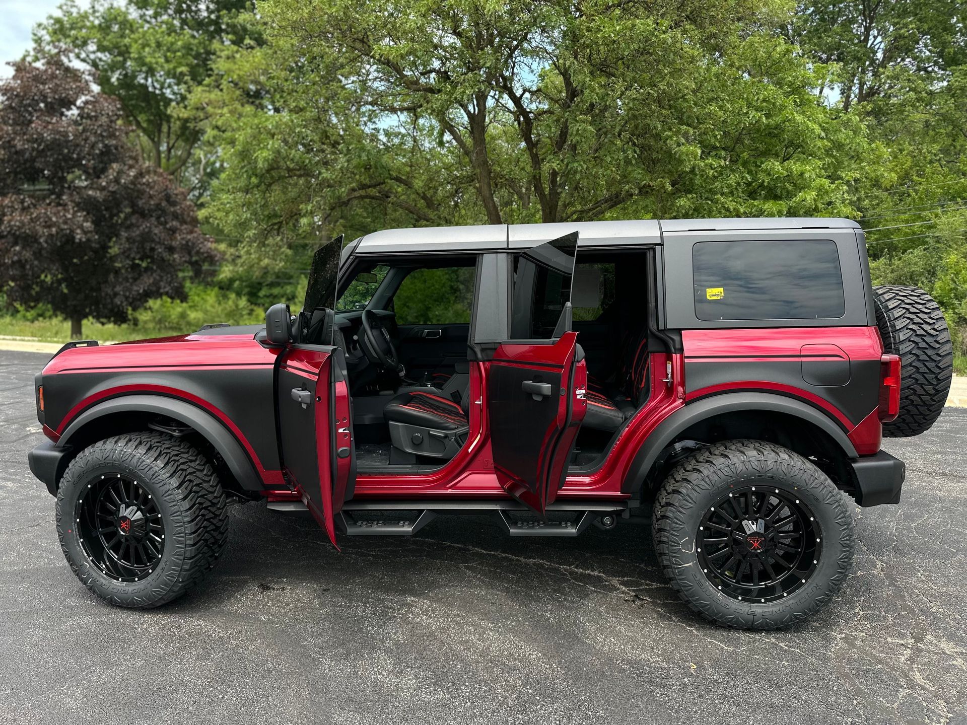 Red off-road SUV with doors open, parked on gravel in a wooded area.