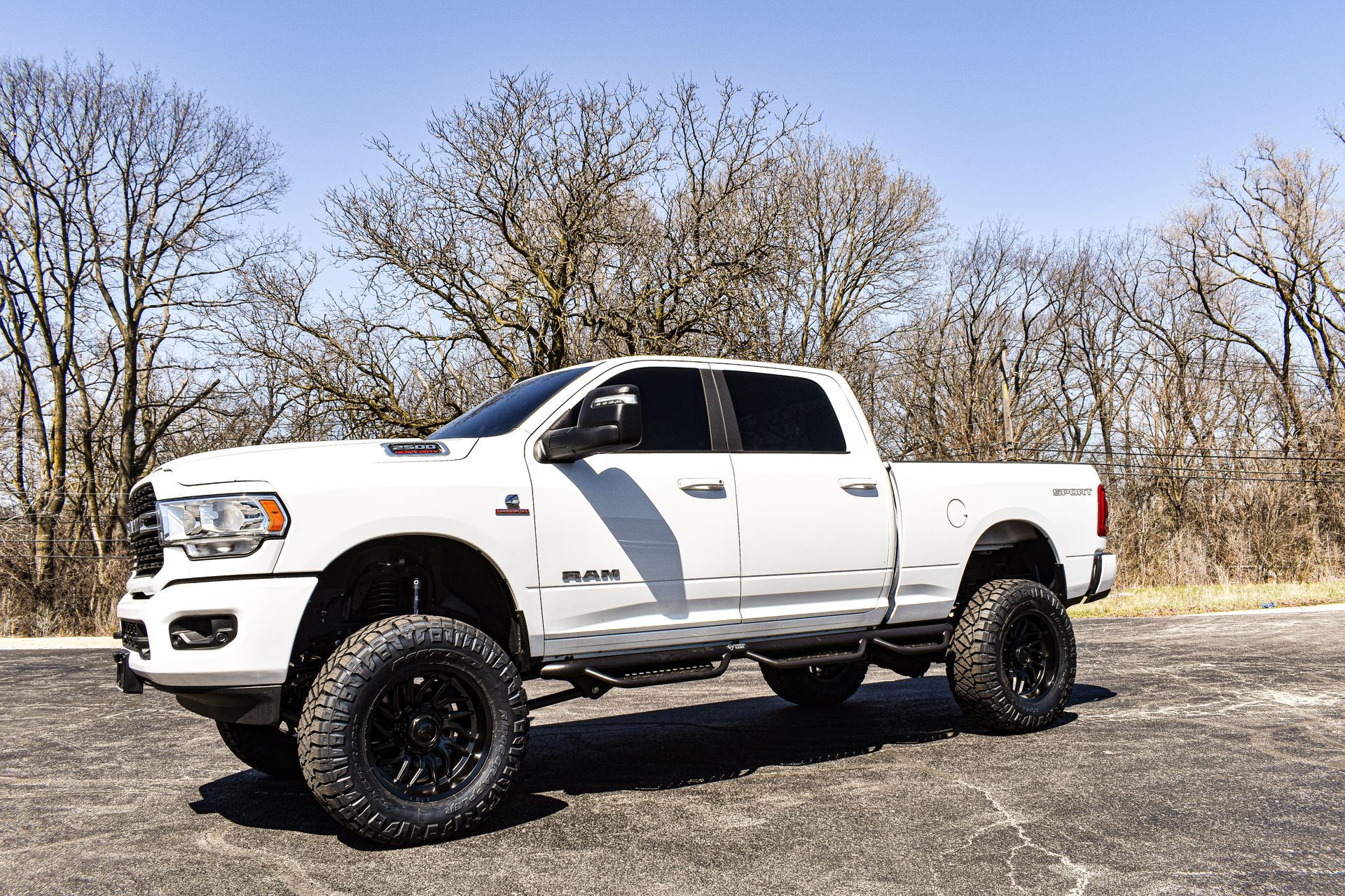 White lifted pickup truck parked outdoors on gravel with leafless trees in the background