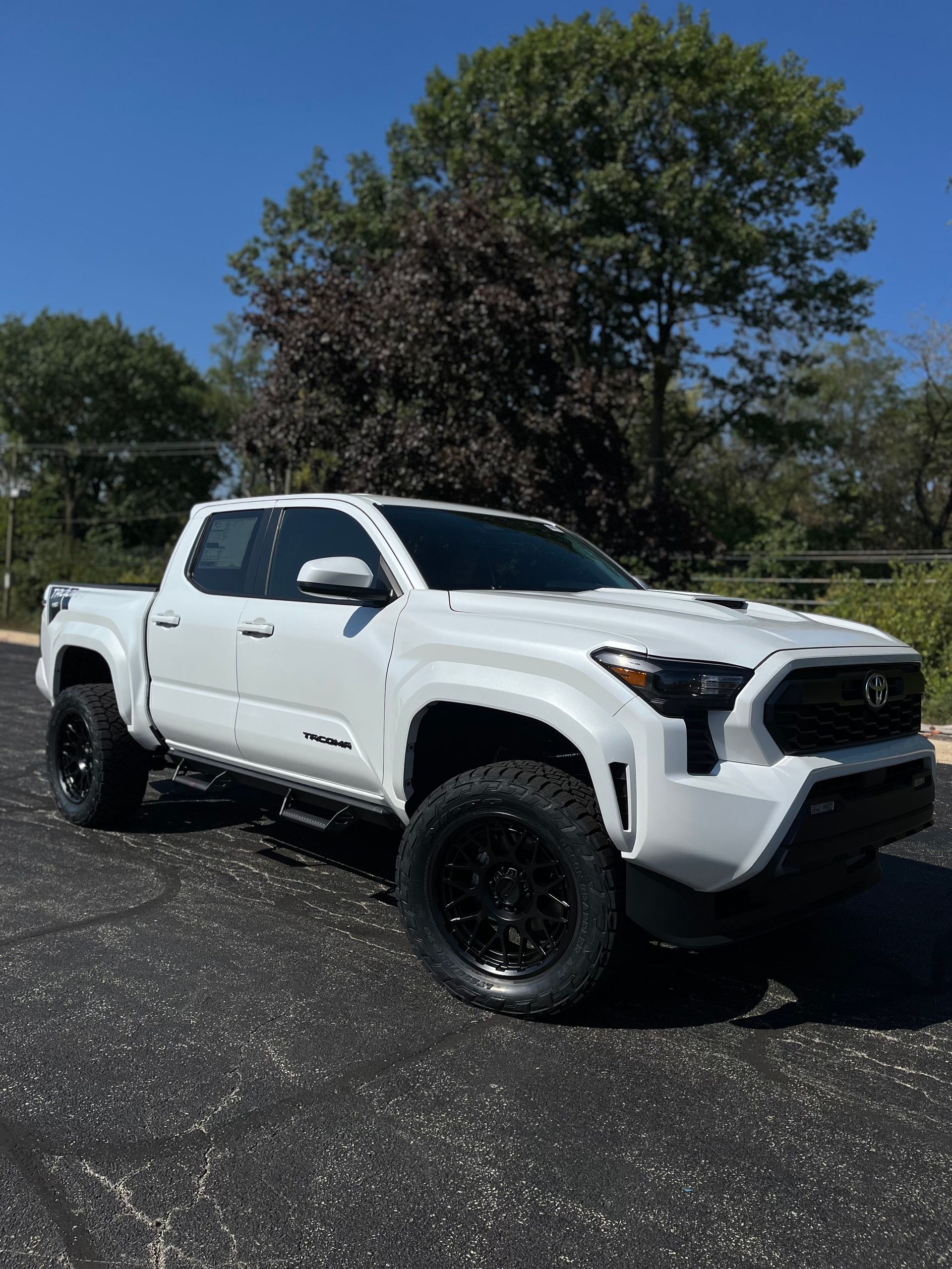 White lifted pickup truck parked on gravel with trees and blue sky in the background