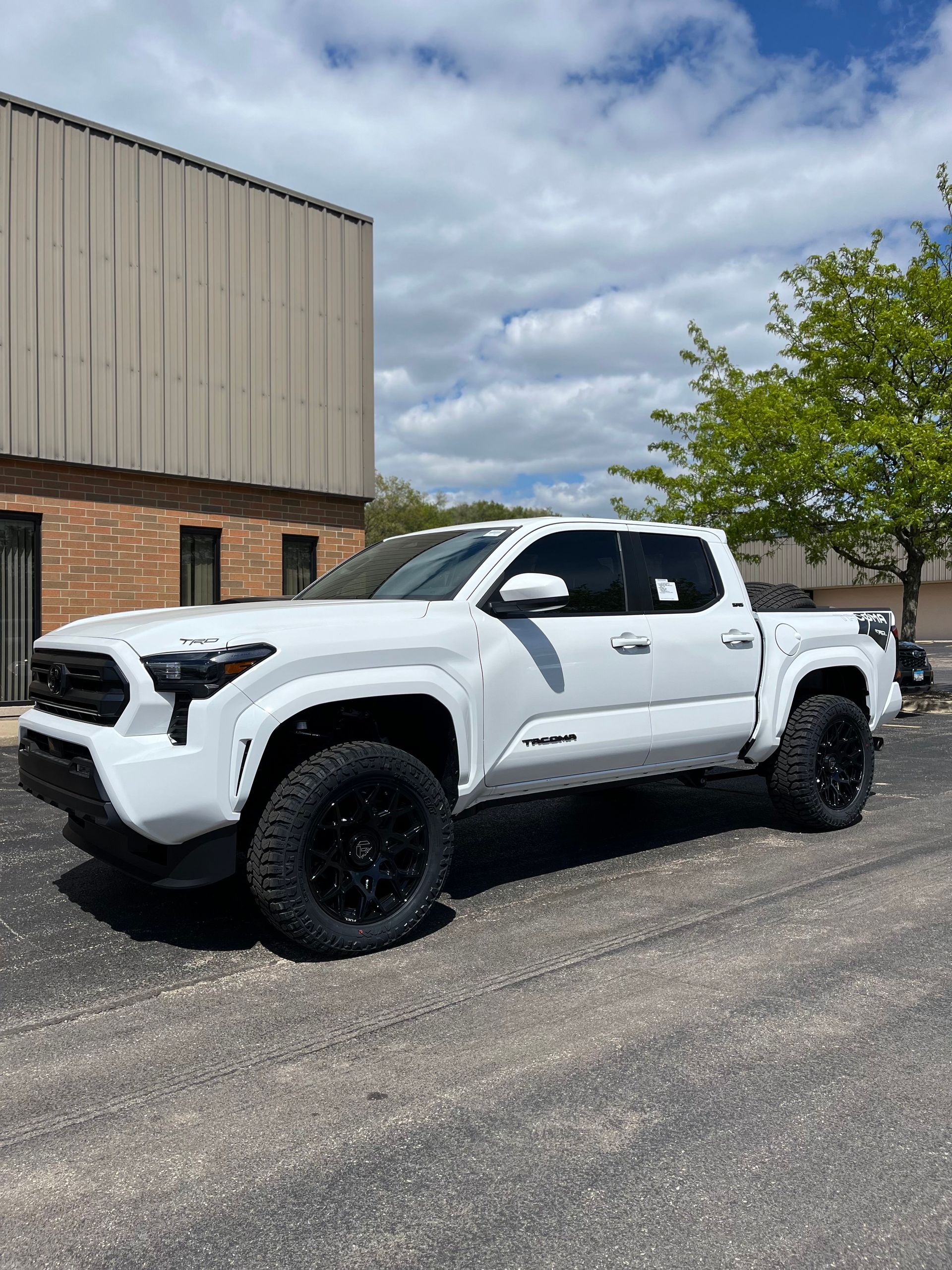 White lifted pickup truck parked beside a brick building under a cloudy sky