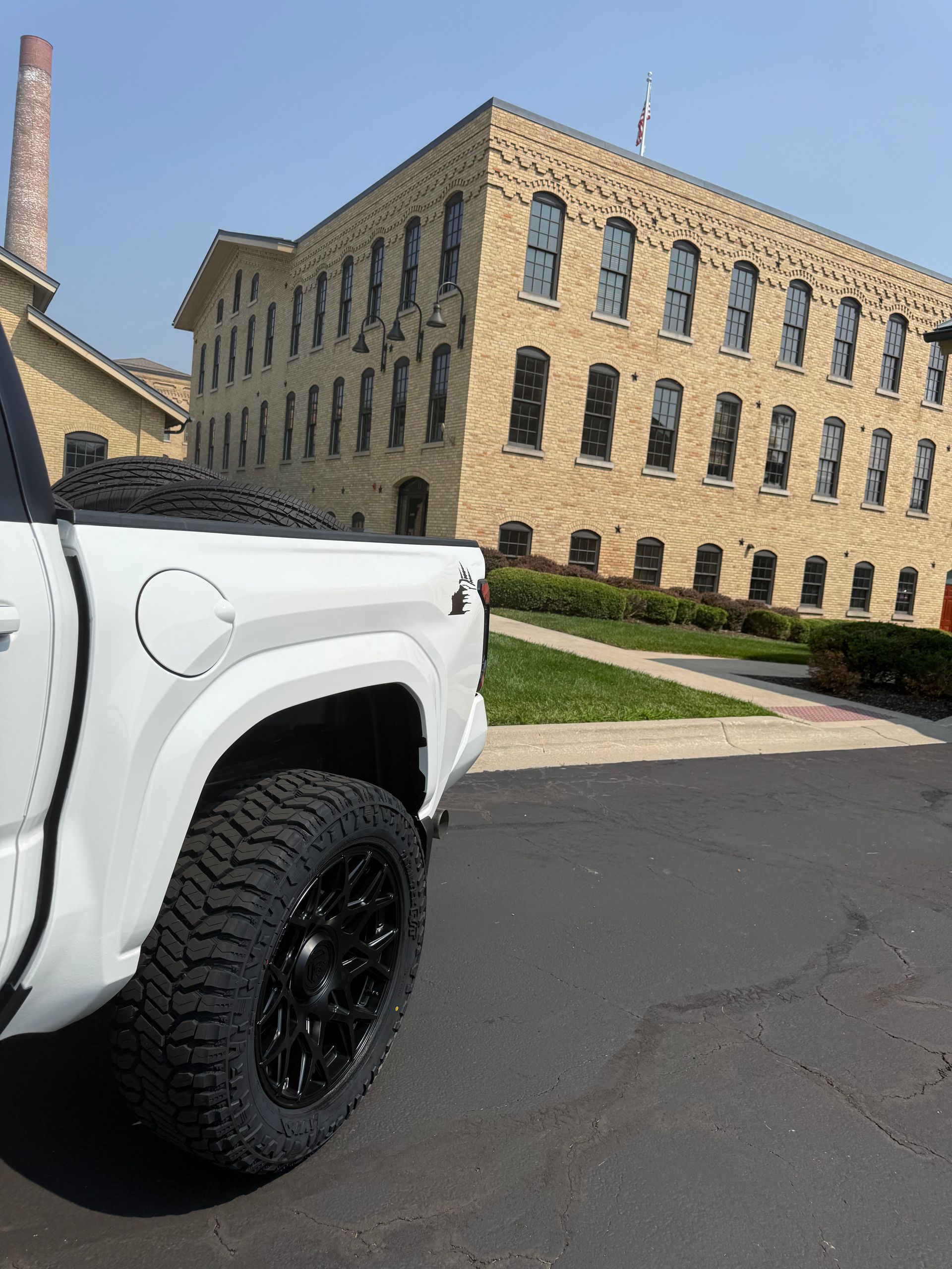 White pickup truck parked by a tan brick building on a sunny street