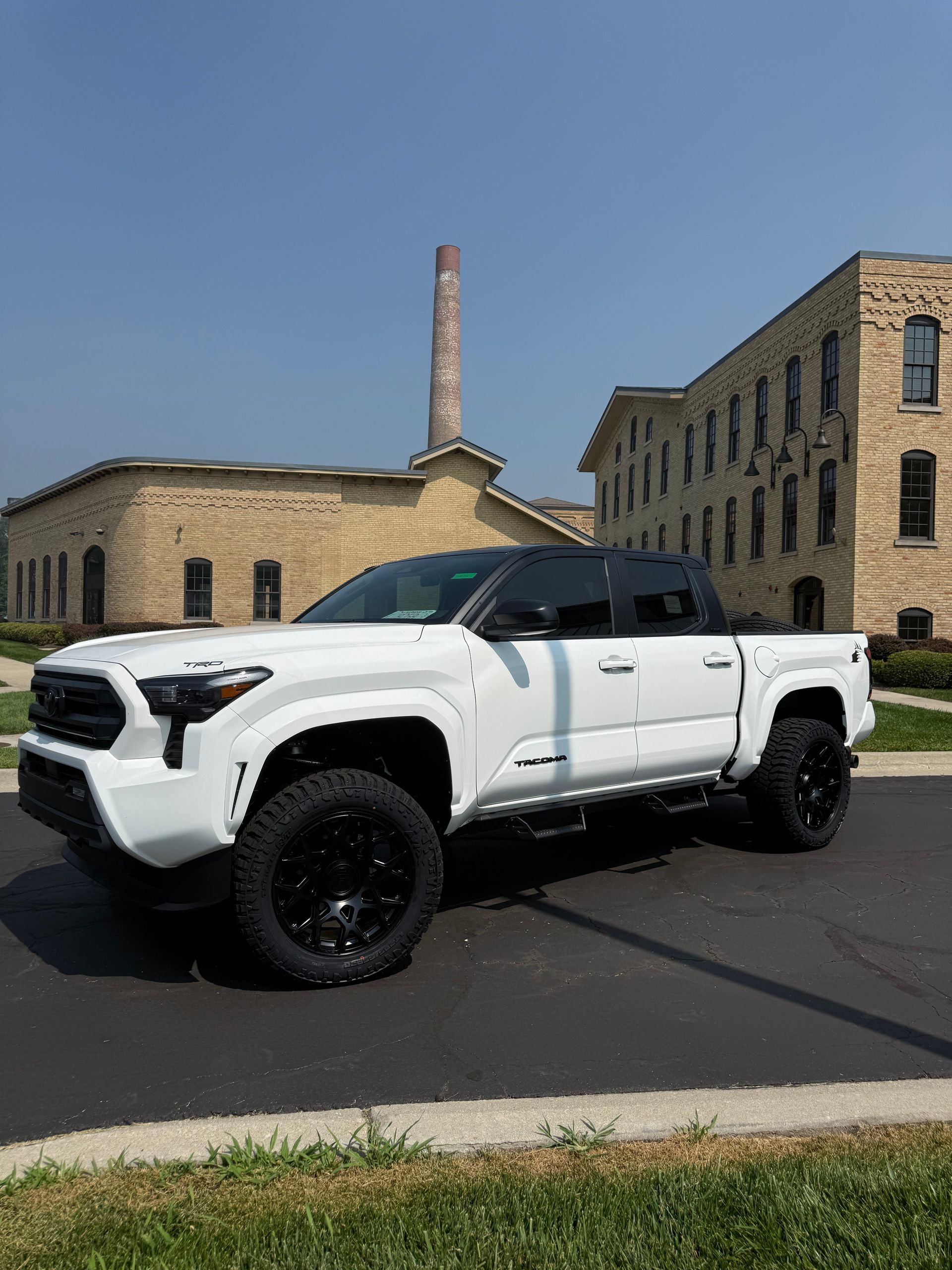 White lifted pickup truck parked on a street in front of stone buildings under a clear blue sky