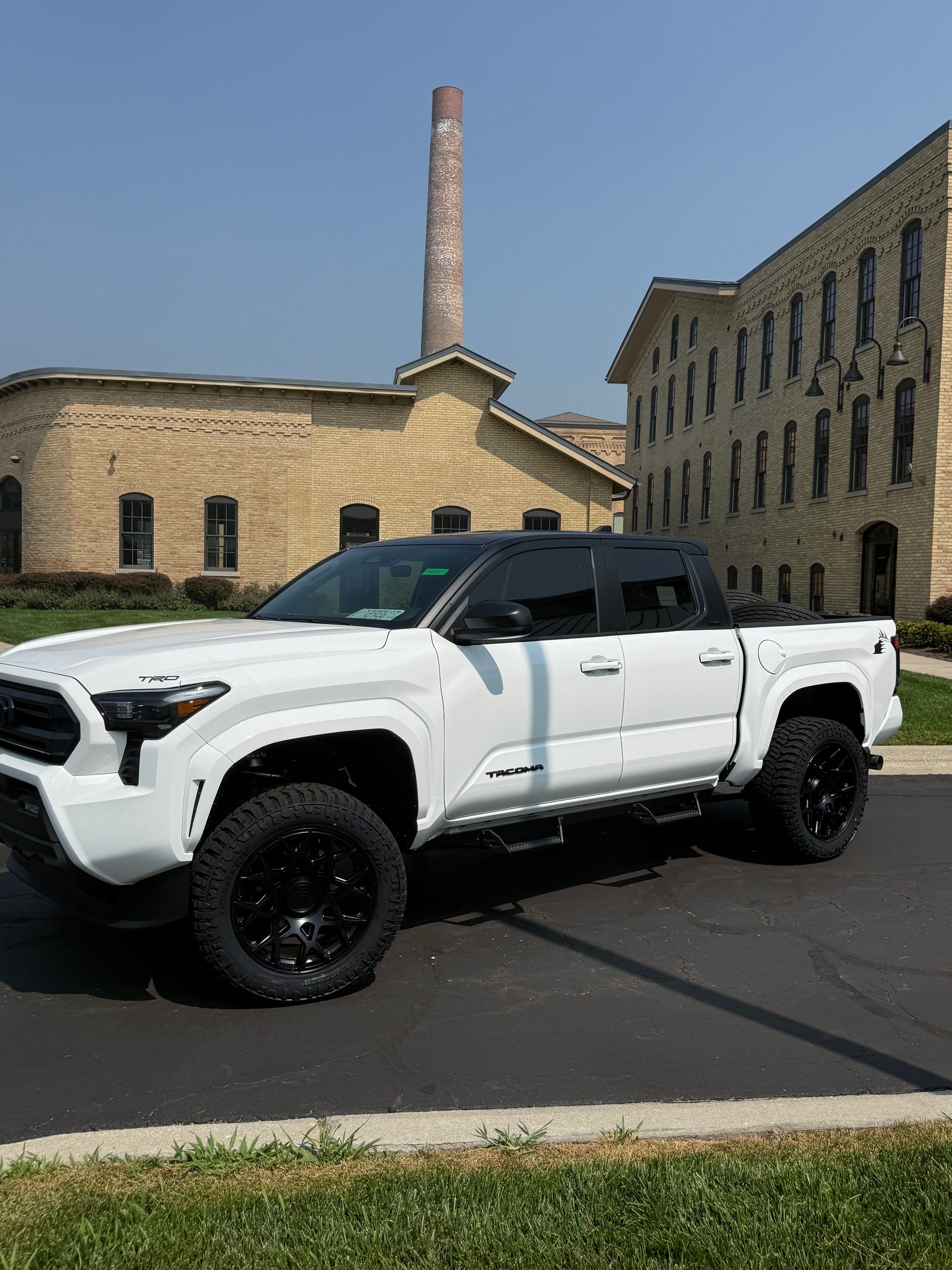 White lifted pickup truck parked outside stone industrial buildings under a clear blue sky
